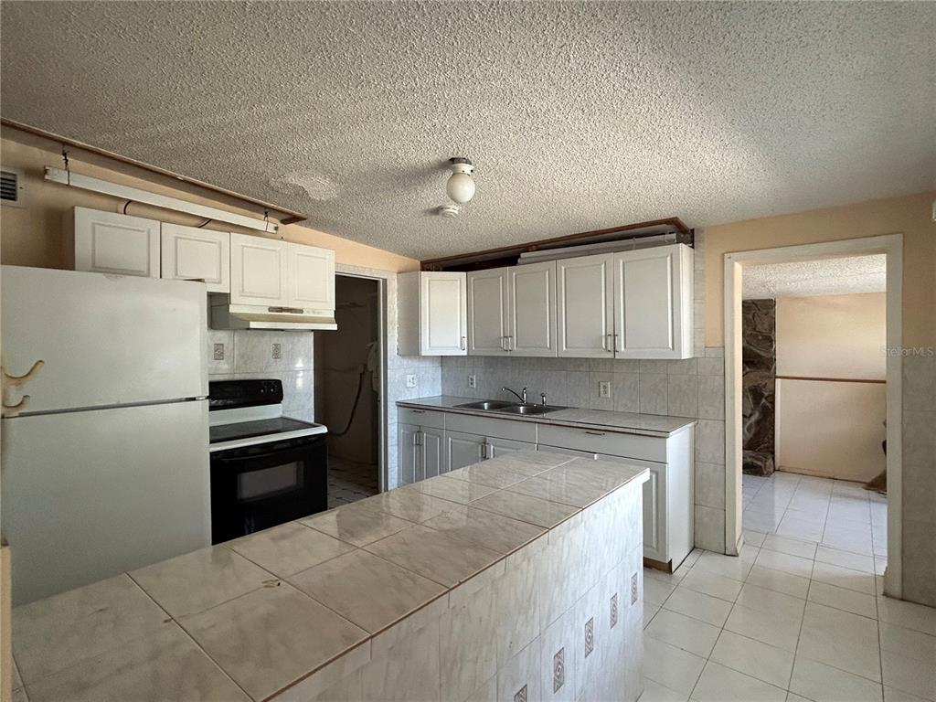 A kitchen features white cabinets, tiled countertops, a white refrigerator, and a tiled floor — 6328 30TH WAY N, ST PETERSBURG, FL
