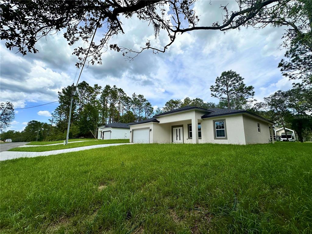A single-story house with a white exterior and a garage stands on a grassy lot — 7977 N POCONO DRIVE, CITRUS SPRINGS, FL