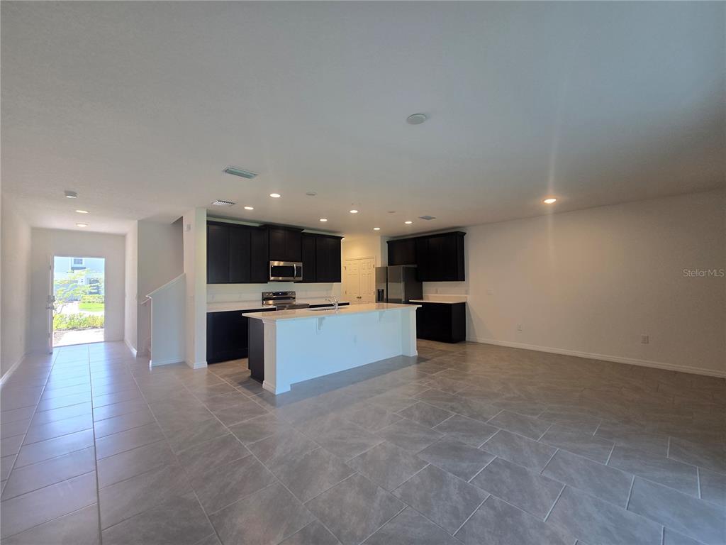 An open-concept kitchen features dark cabinets, a white island, and light-colored tile flooring — 2552 STARRY POINT, ST CLOUD, FL