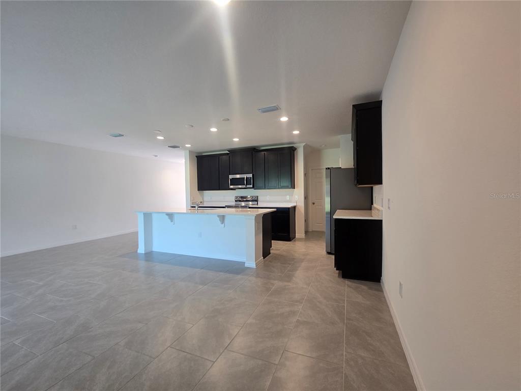 A kitchen features dark cabinets, a white island, and gray tile flooring in an open space — 2552 STARRY POINT, ST CLOUD, FL