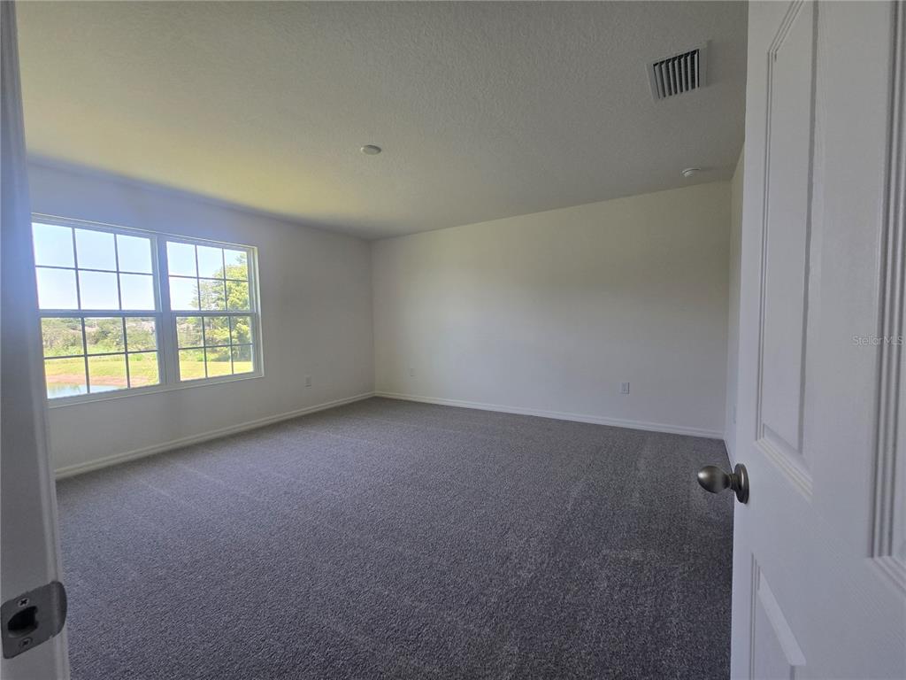 An empty bedroom features gray carpeting, white walls, and a window overlooking a pond — 2552 STARRY POINT, ST CLOUD, FL