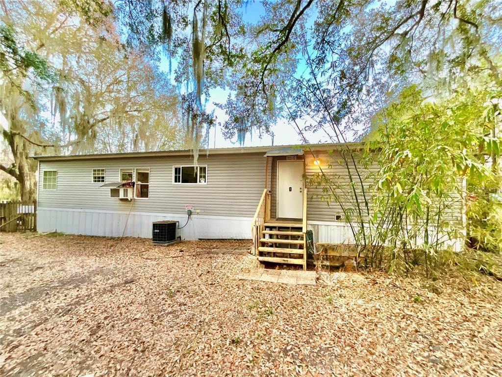 A single-story manufactured home with light gray siding, a wooden staircase, and surrounding trees — 1837 STATE ROAD 20, HAWTHORNE, FL
