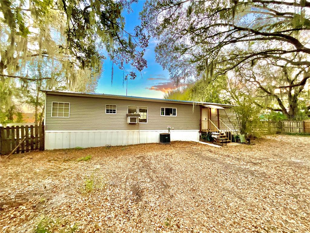 A single-story manufactured home with gray siding sits on a lot covered in fallen leaves — 1837 STATE ROAD 20, HAWTHORNE, FL