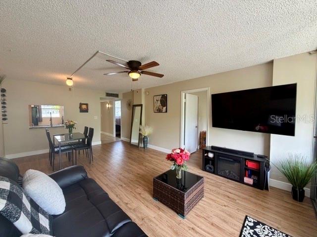 A living room features wood-look flooring, a ceiling fan, and a wall-mounted television — 107 ROYAL PARK DRIVE UNIT 2G, OAKLAND PARK, FL
