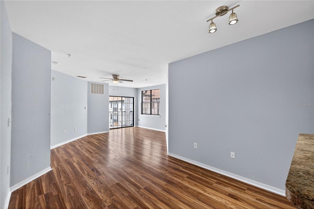 An empty living room features light blue walls, wood-look flooring, a ceiling fan, and a balcony — 5550 E MICHIGAN STREET UNIT 3306, ORLANDO, FL