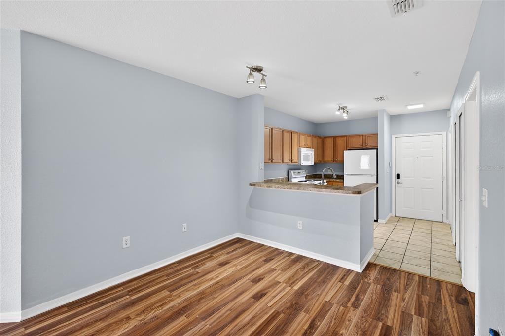 A dining area with wood-look flooring opens to a kitchen with wood cabinets and appliances — 5550 E MICHIGAN STREET UNIT 3306, ORLANDO, FL