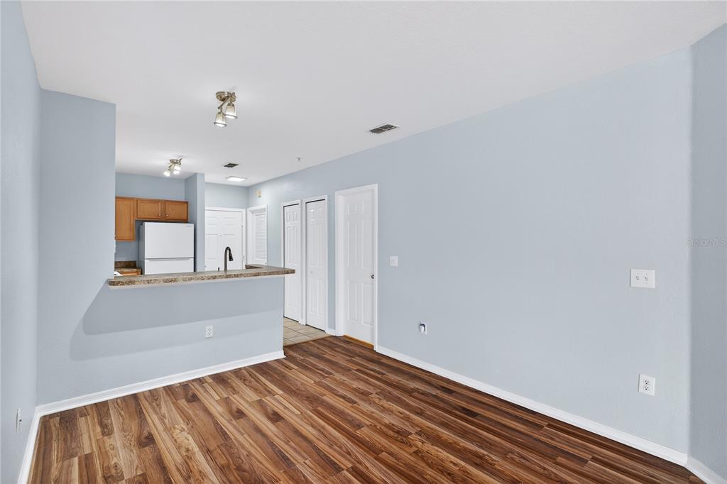 A living area with light blue walls, wood-look flooring, and a breakfast bar kitchen pass-through — 5550 E MICHIGAN STREET UNIT 3306, ORLANDO, FL