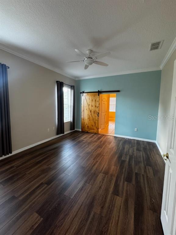 A bedroom features dark wood-look flooring, a ceiling fan, and a wooden sliding barn door — 8821 SW 82ND COURT ROAD, OCALA, FL