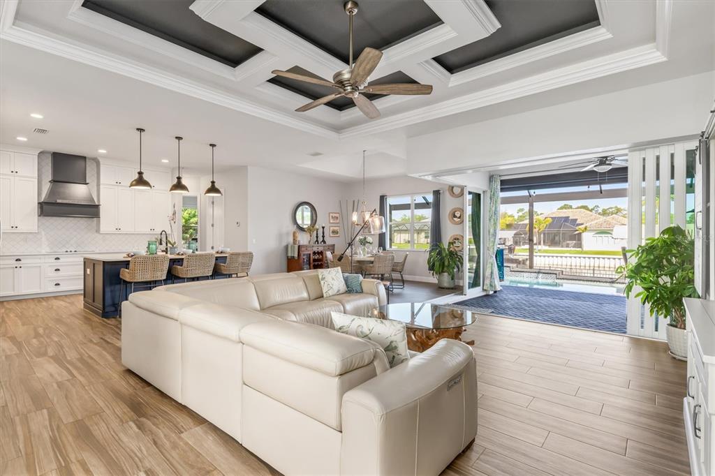An open-concept living room features a coffered ceiling, light wood floors, and sliding glass doors — 8407 DAFOE STREET, PORT CHARLOTTE, FL