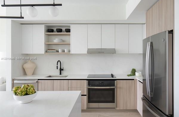 A modern kitchen features white upper cabinets, light wood lower cabinets, and stainless steel appliances — 3900 Alton Road # 305, Miami Beach FL 33140, MIAMI BEACH, FL