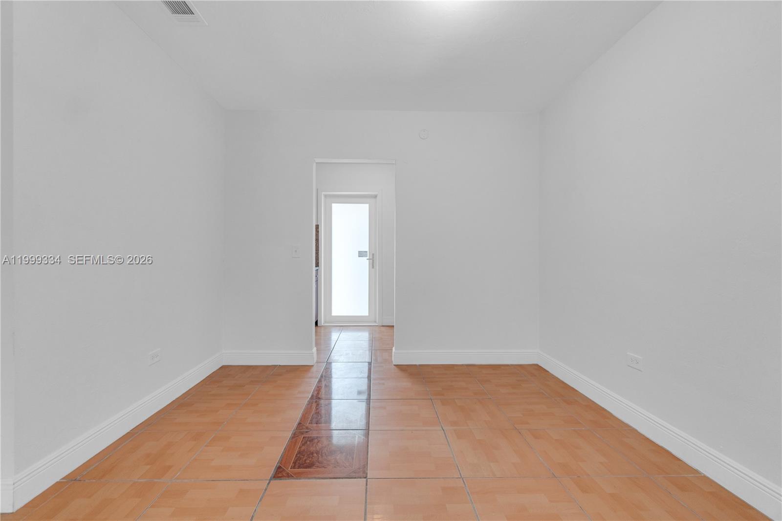 An empty room features light-colored walls, tiled flooring with a decorative center strip, and a doorway — 1730 NW 55th Ter # 1730, Miami FL 33142, MIAMI, FL