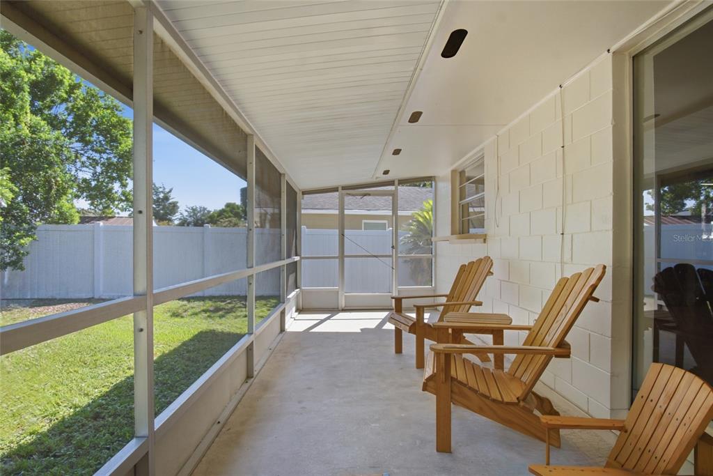 A screened-in porch features a concrete floor, white block walls, and three wooden chairs — 1420 AVALON BOULEVARD, CASSELBERRY, FL