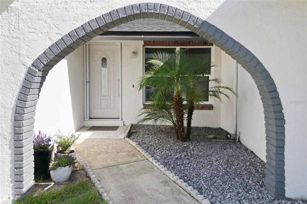 A white front door is framed by a gray brick archway leading to a small garden — 1420 AVALON BOULEVARD, CASSELBERRY, FL