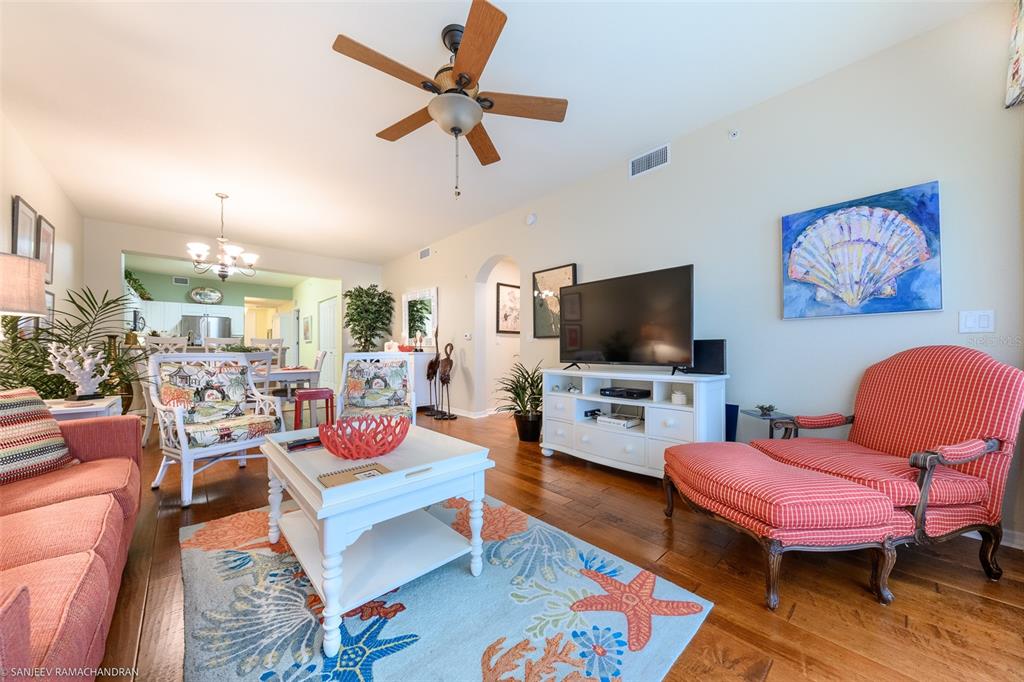 A living room features hardwood floors, a white coffee table, a television, and coastal decor — 5119 MELBOURNE STREET UNIT C-201, PORT CHARLOTTE, FL