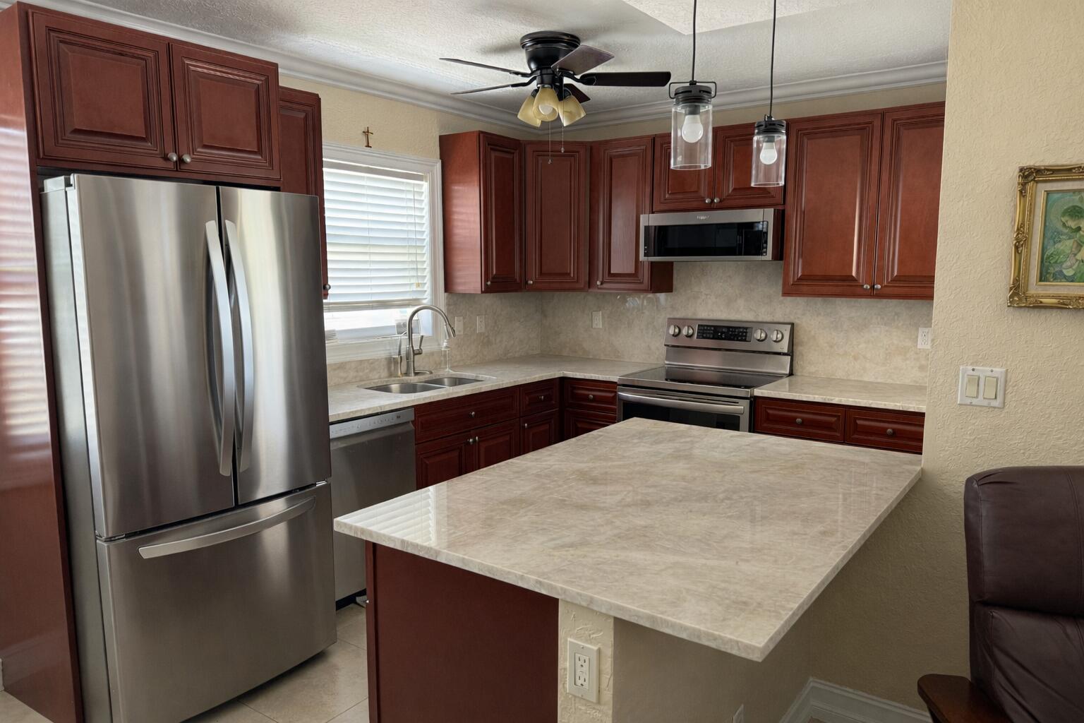 A kitchen with cherry wood cabinets, stainless steel appliances, and a light-colored stone countertop island — 1221 SE 3rd Street # 4, Deerfield Beach FL 33441, DEERFIELD BEACH, FL