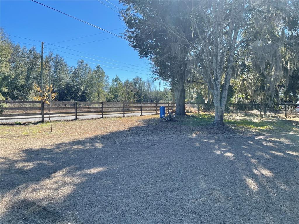 A grassy yard features a wooden fence, a large tree, and a blue water tank — 4456 NW 44TH AVENUE, OCALA, FL