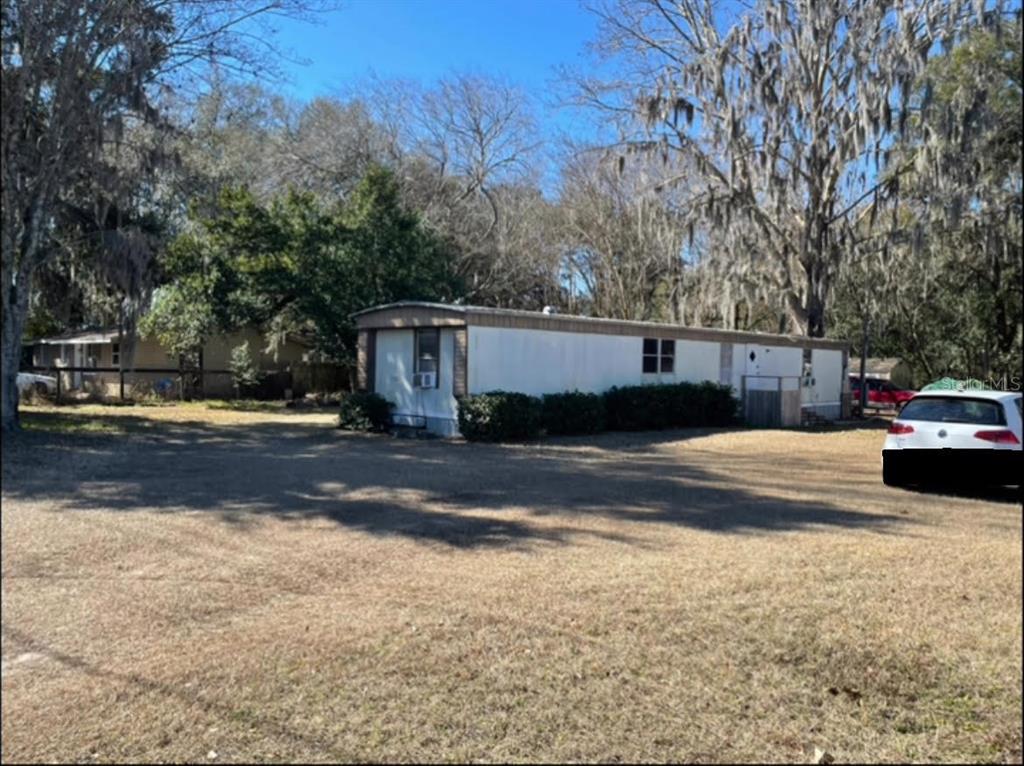 A single-wide mobile home sits on a large, grassy lot surrounded by mature trees — 4456 NW 44TH AVENUE, OCALA, FL