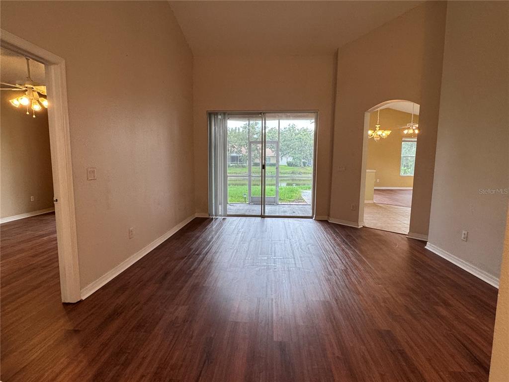 An empty living room features wood-look flooring, vaulted ceilings, and a sliding glass door — 10207 QUAILS LANDING AVENUE, TAMPA, FL