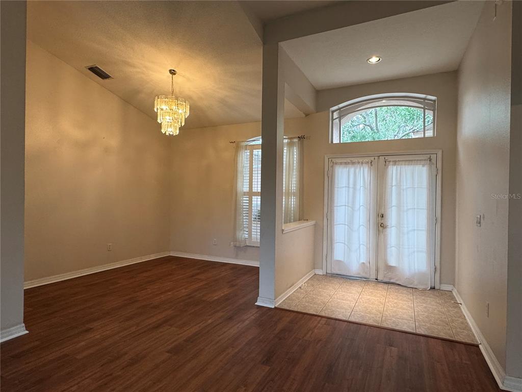 A dining room with wood flooring and a chandelier sits next to a tiled entryway — 10207 QUAILS LANDING AVENUE, TAMPA, FL