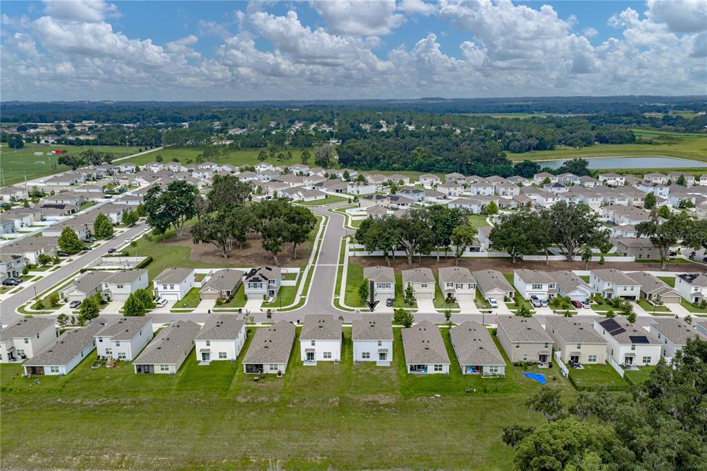 An aerial view shows a suburban neighborhood with rows of houses and a grassy field — 13648 WHISKEY DAISY DRIVE, DADE CITY, FL
