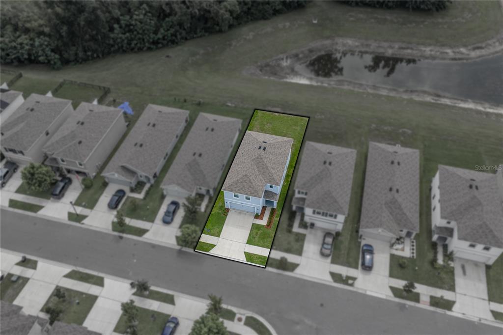 An aerial view shows a blue two-story house with a fenced backyard facing a pond — 13648 WHISKEY DAISY DRIVE, DADE CITY, FL