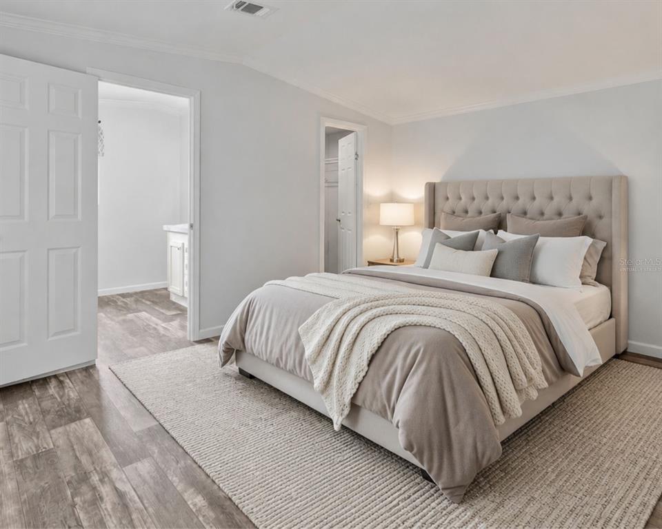 A bedroom features a tufted beige headboard, neutral bedding, and wood-look flooring — 3035 CRYSTAL HILLS DRIVE, LAKELAND, FL