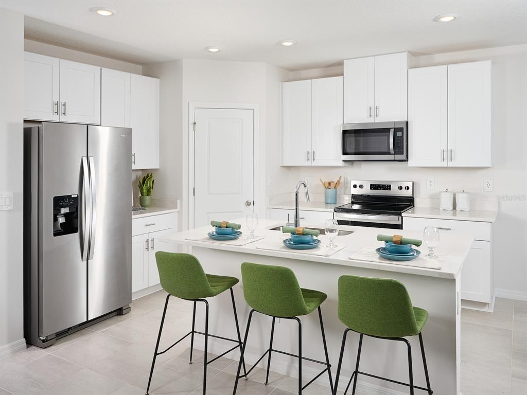 A modern kitchen features white cabinets, stainless steel appliances, a center island, and green stools — 13718 UMBER FOREST STREET, HUDSON, FL