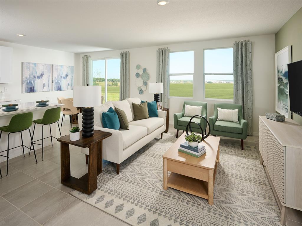 A bright living room features a sofa, two green armchairs, a coffee table, and dining area — 13718 UMBER FOREST STREET, HUDSON, FL