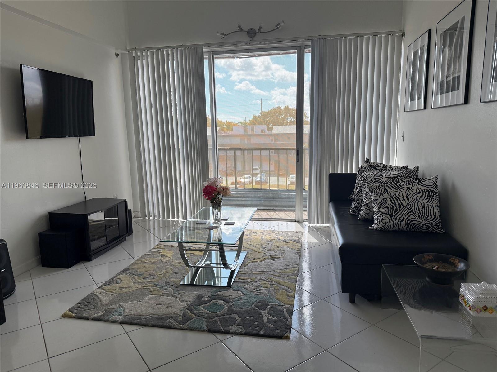 A living room features a black sofa, glass coffee table, area rug, and balcony access — 8821 W Flagler St # 411, Miami FL 33174, MIAMI, FL