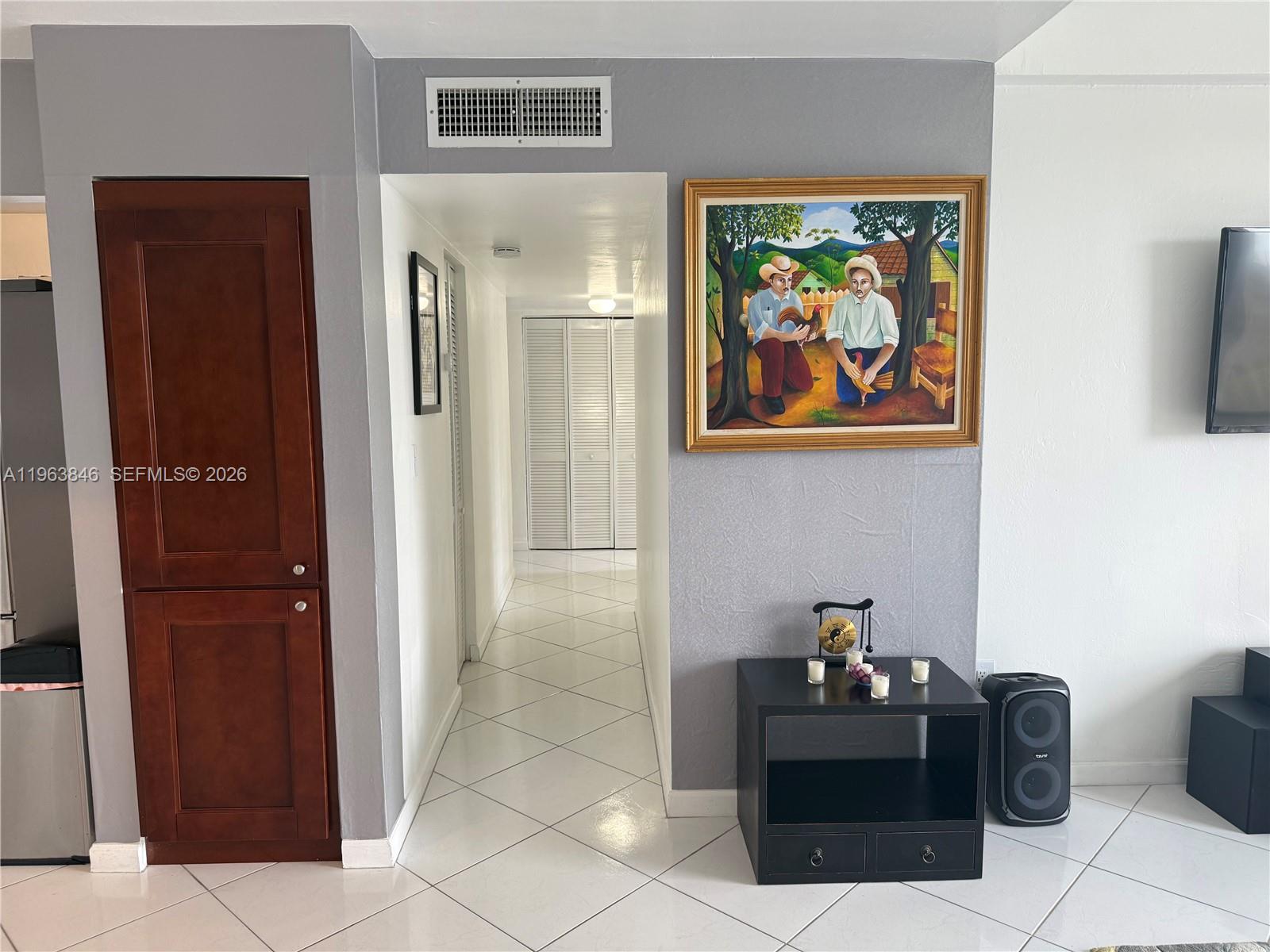 A hallway with white tile floors leads to a closet between a wooden cabinet and a painting — 8821 W Flagler St # 411, Miami FL 33174, MIAMI, FL