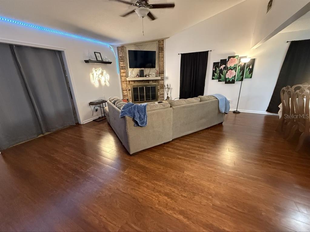 A living room features wood flooring, a corner fireplace with a television, and a sectional sofa — 35058 WHISPERING OAKS BOULEVARD, DADE CITY, FL