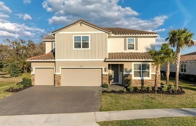A two-story suburban house with a tan exterior, a multi-car garage, and a tiled roof — 7284 GREAT EGRET BOULEVARD, SARASOTA, FL