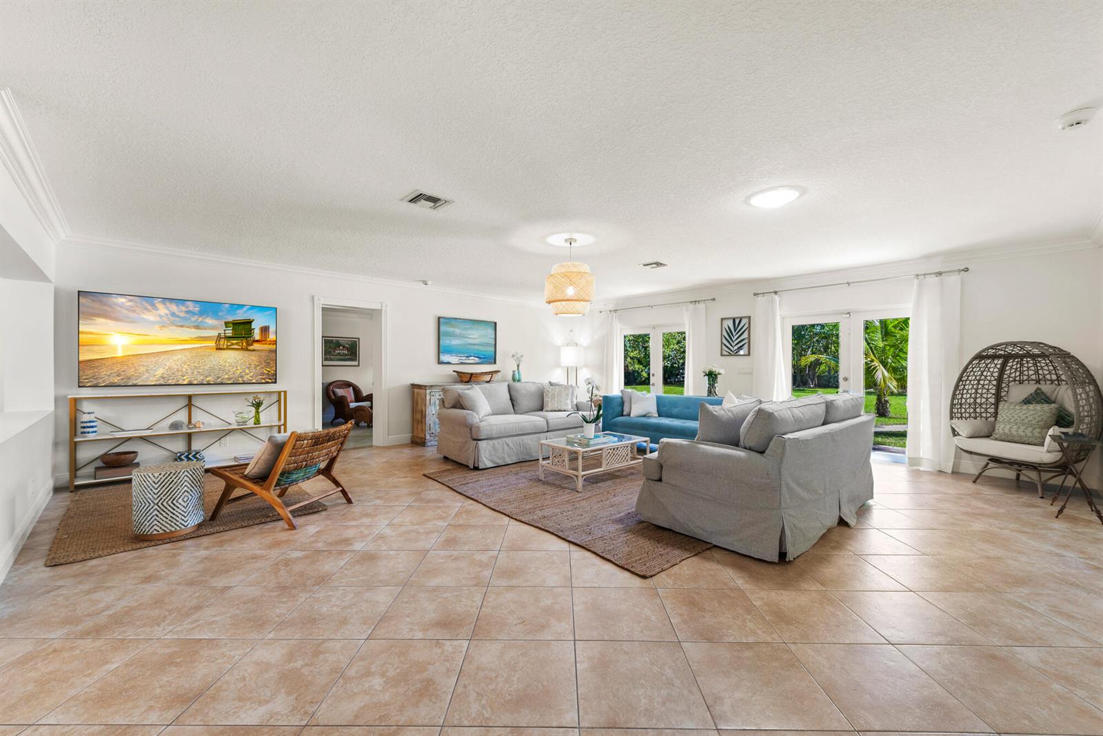 A spacious living room features tile floors, multiple sofas, a television, and large glass doors — 602 N Atlantic Drive, Lantana FL 33460, LANTANA, FL