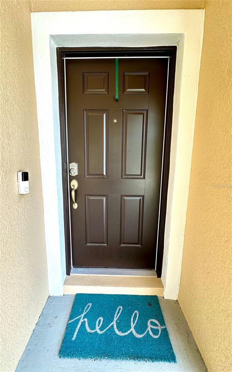A dark brown front door with a doorbell camera and a teal hello doormat — 4247 ANGELICA LOOP, WESLEY CHAPEL, FL