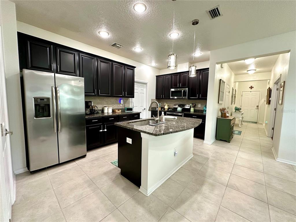 A kitchen features dark wood cabinets, granite countertops, a center island, and stainless steel appliances — 4247 ANGELICA LOOP, WESLEY CHAPEL, FL