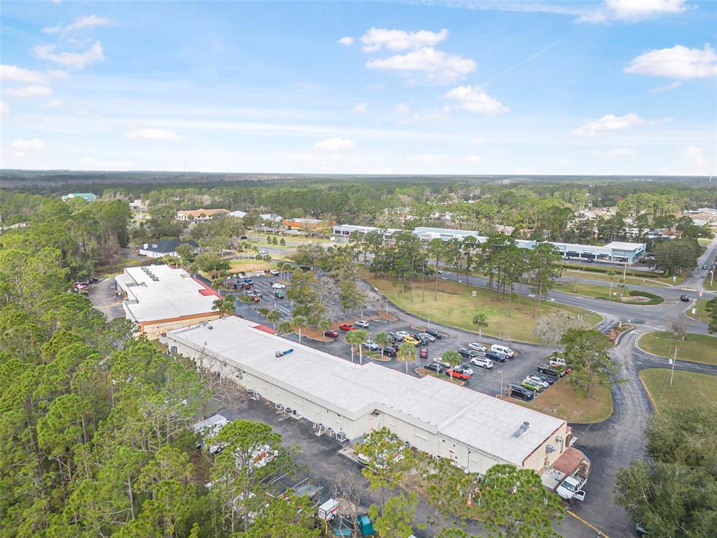 An aerial view shows a commercial building with a large parking lot near trees — 223 ST. JOE PLAZA, PALM COAST, FL
