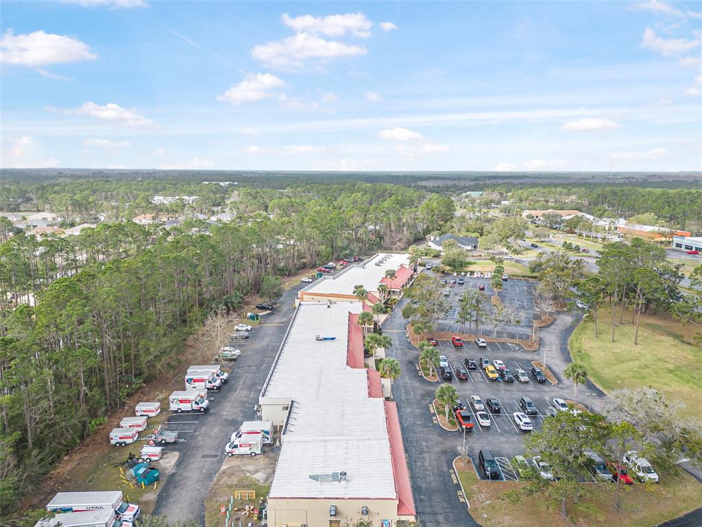 An aerial view shows a commercial strip mall with a large parking lot and surrounding woods — 223 ST. JOE PLAZA, PALM COAST, FL