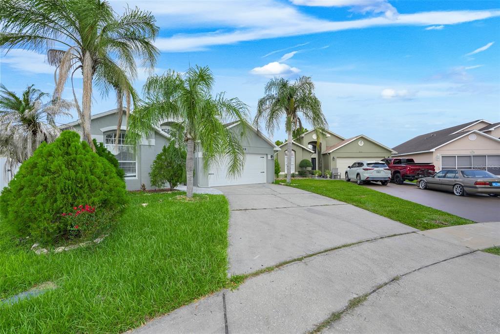A single-story house with a concrete driveway, palm trees, and a green lawn — 2109 CARBINE COURT, KISSIMMEE, FL