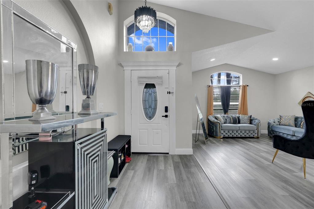 An entryway with light gray wood-look flooring, a white front door, and a crystal chandelier — 2109 CARBINE COURT, KISSIMMEE, FL