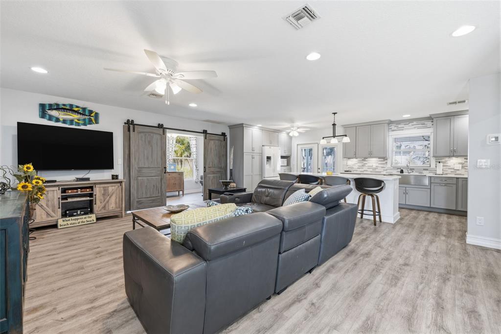 An open-concept living room and kitchen featuring grey cabinetry, wood-look flooring, and sliding barn doors — 4339 50TH AVENUE S, ST PETERSBURG, FL