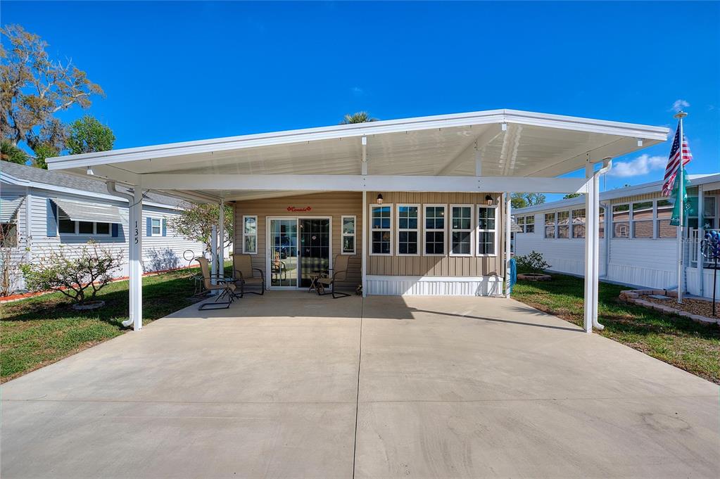 A mobile home exterior features a large concrete carport and a tan facade with windows — 135 CITRUS RIDGE DRIVE, DAVENPORT, FL
