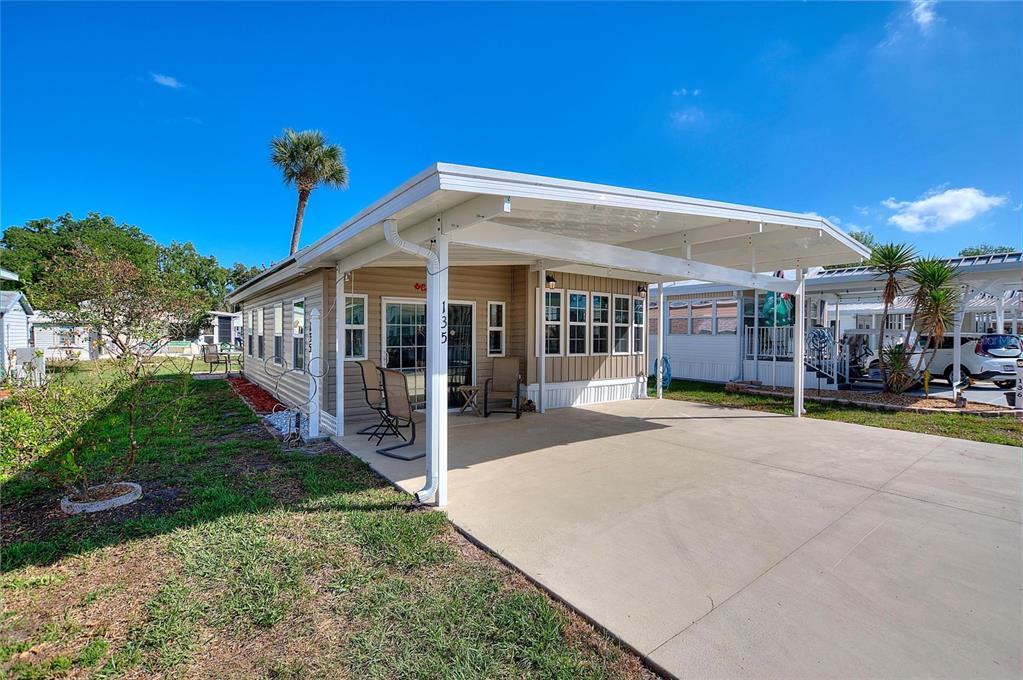 A single-story mobile home features a tan exterior, a concrete driveway, and a covered carport — 135 CITRUS RIDGE DRIVE, DAVENPORT, FL