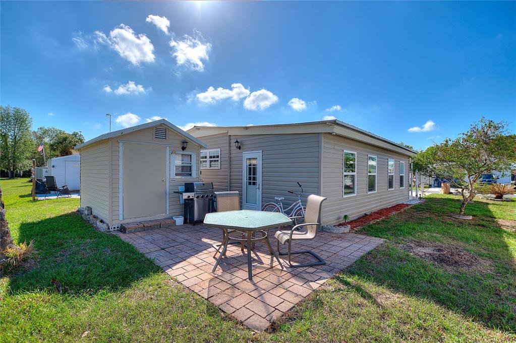 A tan mobile home exterior features a brick patio, a storage shed, and a bicycle — 135 CITRUS RIDGE DRIVE, DAVENPORT, FL