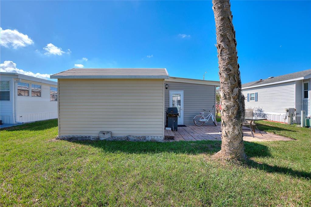 A beige mobile home exterior features a small patio, a bicycle, and a palm tree — 135 CITRUS RIDGE DRIVE, DAVENPORT, FL