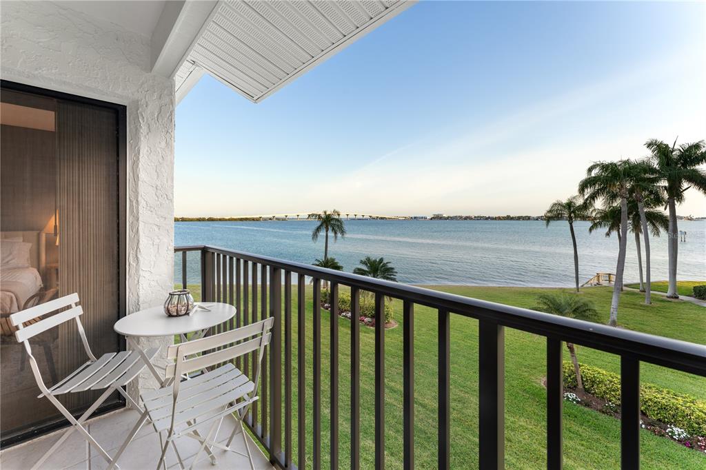A balcony with a small table and chairs overlooks a grassy lawn and the bay — 6287 BAHIA DEL MAR CIRCLE UNIT 312, ST PETERSBURG, FL