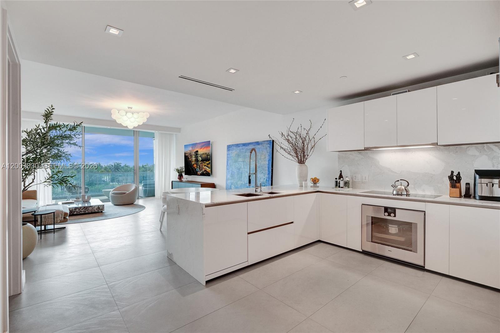 A modern open-concept kitchen features white cabinetry, marble countertops, and a view of a balcony — 10201 Collins Ave # 404, Bal Harbour FL 33154, BAL HARBOUR, FL