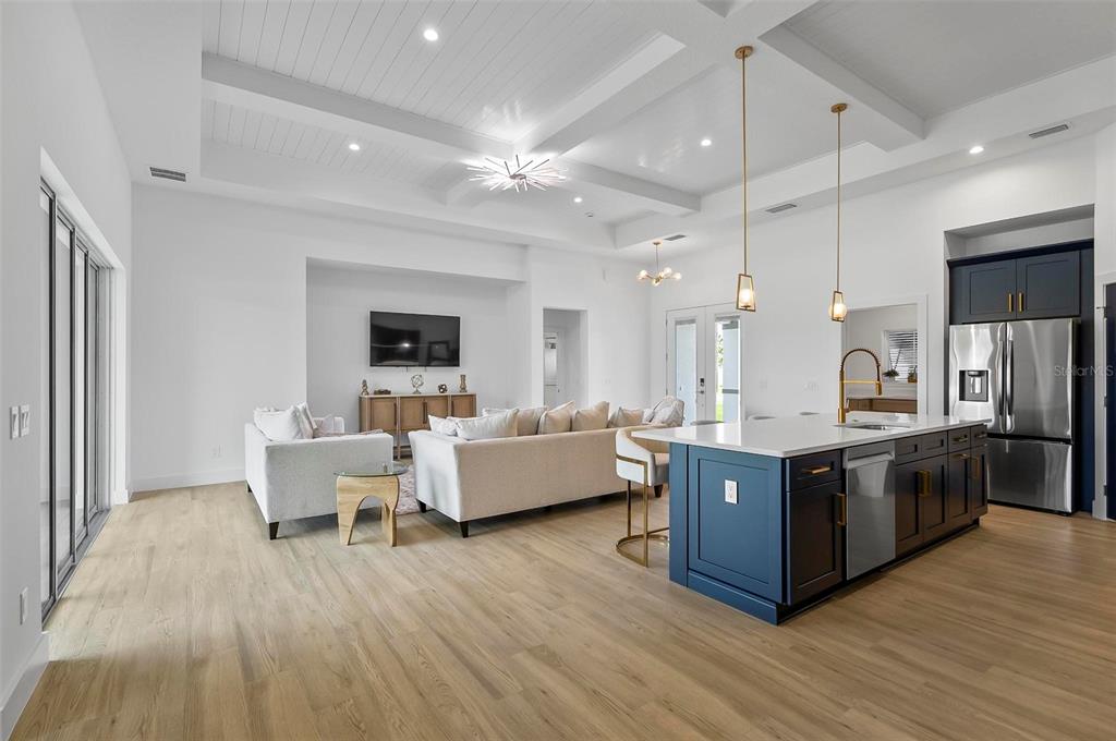 An open-concept living room and kitchen featuring light wood floors, white cabinetry, and blue accents — 1 CLEMENTON LANE, PALM COAST, FL