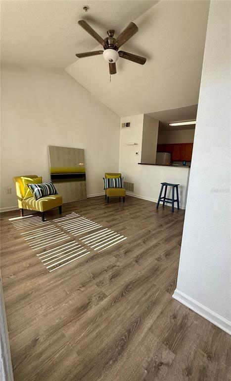 A living room with wood-look flooring, a ceiling fan, two yellow chairs, and a breakfast bar — 4802 51ST STREET W UNIT 623, BRADENTON, FL