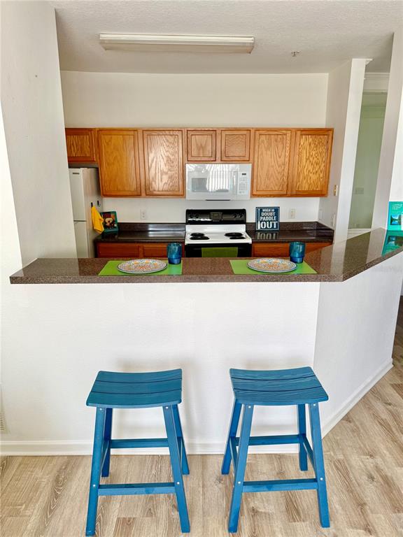 A kitchen features wood cabinets, a white microwave, a stove, and a breakfast bar with stools — 4802 51ST STREET W UNIT 623, BRADENTON, FL