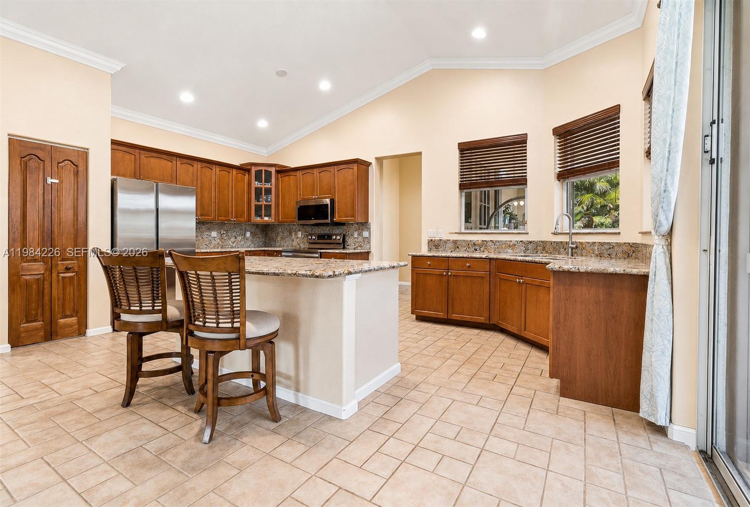 A kitchen features wood cabinets, granite countertops, a central island, and tile flooring — 5026 Coconut Blvd, Palm Beach FL 33411, PALM BEACH, FL